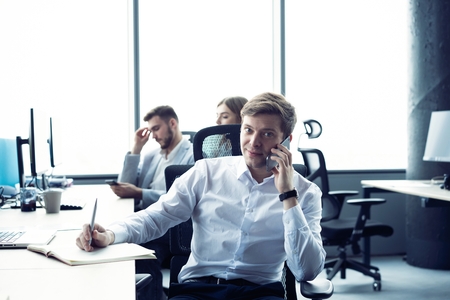 Cheerful man in office answering the phone.の写真素材