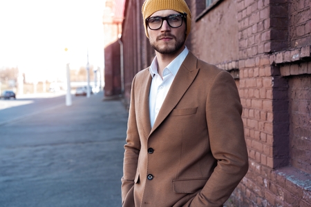 Portrait of stylish handsome young man in glasses with bristle standing outdoors. Man wearing jacket and shirt.の写真素材