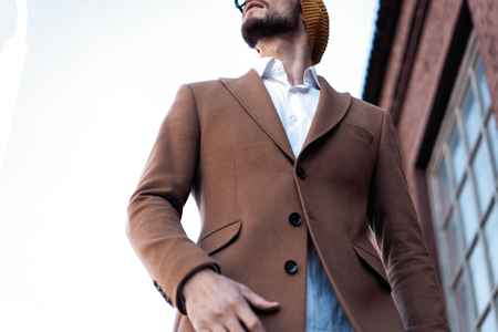 Portrait of stylish handsome young man in glasses with bristle standing outdoors. Man wearing jacket...