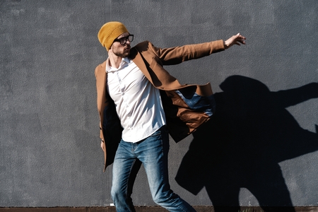 Portrait of handsome bearded man dressed in fashionable clothes standing on street against gray wall backgroundの写真素材