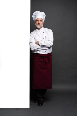 Full length portrait of a happy chef cook showing copyspace on the palms isolated on black background.の写真素材