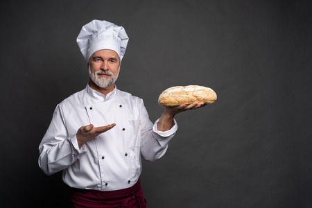 Male baker holding bread loaf and looking at camera isolated on black.の写真素材