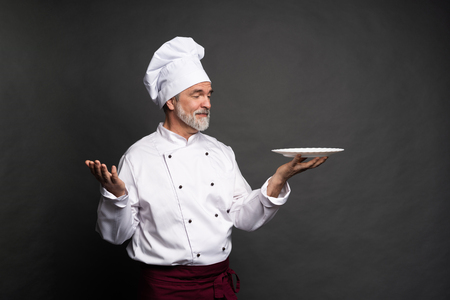 Mature cook chef holding an empty plate on a black background.の写真素材