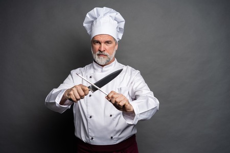 Portrait of a mature chef cook holding knifes isolated on a black background.の写真素材