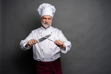 Portrait of a mature chef cook holding knifes isolated on a black background.の写真素材