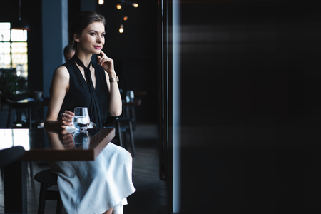 Portrait of gorgeous female drinking tea or coffee and looking with smile out of the coffee shop window while enjoying her leisure timeの写真素材