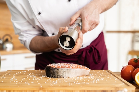The chef prepares fresh fish salmon, trout, sprinkles with sea salt and vegetables. Horizontal photo. Concept cooking healthy and vegan cuisine, clean food, restaurants, hotel business.の写真素材