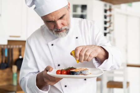Chef with diligence finishing dish on plate, fish with vegetablesの写真素材