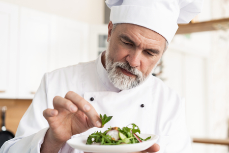 male cook chef decorating garnishing prepared salad dish on the plate in restaurant commercial kitchen.の写真素材