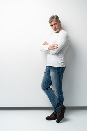 Full body portrait of relaxed mature man standing with arms crossed over white background.の写真素材