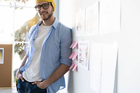 Portrait of a casually dressed young businessman wearing glasses and standing in a trendy office.の写真素材