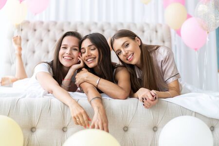 Pajama party. Attractive young smiling women in pajamas drinking champagne while having a slumber party in the bedroom.の写真素材