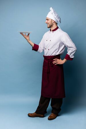 Happy male chef cook standing with plate isolated on light blue background.の写真素材