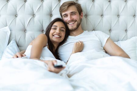 happy couple with remote lying in bed at home and watching tv.の写真素材