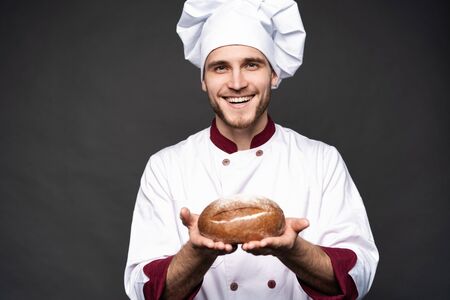 Male baker holding bread loaf and looking at camera isolated on black.の写真素材