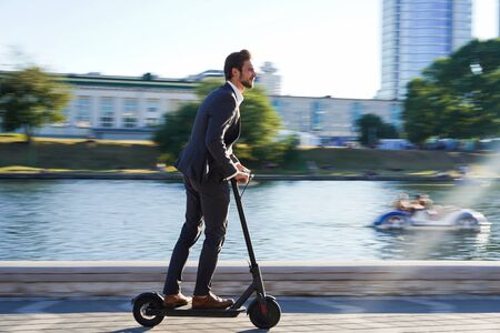 Young business man in a suit riding an electric scooter on a business meeting.の写真素材