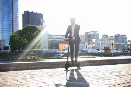 Young business man in a suit riding an electric scooter on a business meeting.の写真素材