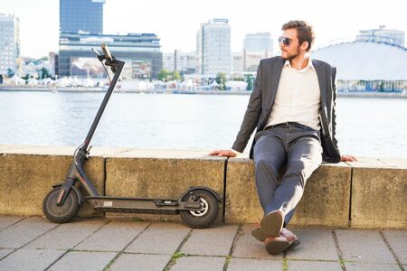 Young modern man using electric scooter on city street. Modern and ecological transportation concept.の写真素材