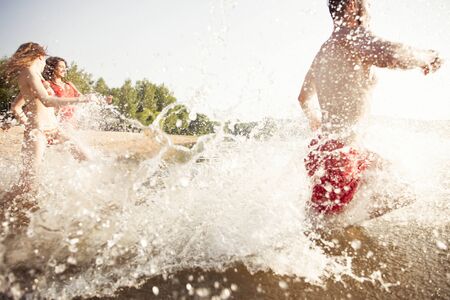 Group of happy friends running in to water - active people having fun on the beach on vacationの写真素材