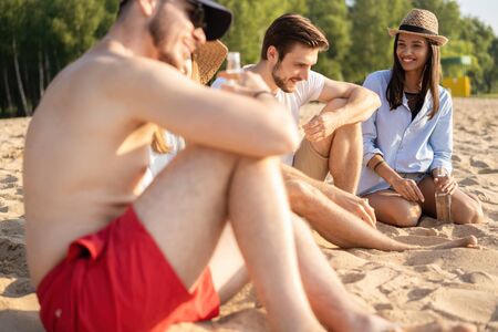 Group of happy young people sitting together at the beach talking and drinking beersの写真素材