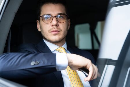 Young businessman sitting on back seat of the car, while his chauffeur is driving automobile.の写真素材