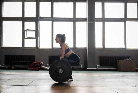 Attractive strong muscular female bodybuilder doing heavy duty squats lifting barbell at the crossfit gymの写真素材