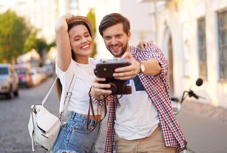 Happy couple of tourists photographing a selfie in a city street in a sunny day.