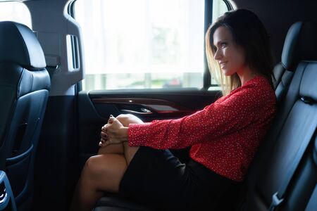Beautiful businesswoman is sitting on back seat of the car.
