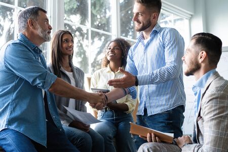 Welcome to our team! Business men in smart casual wear shaking hands while working in the creative office.の写真素材