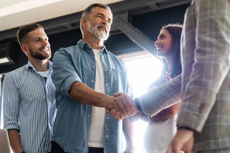 Welcome to our team! Business men in smart casual wear shaking hands while working in the creative...