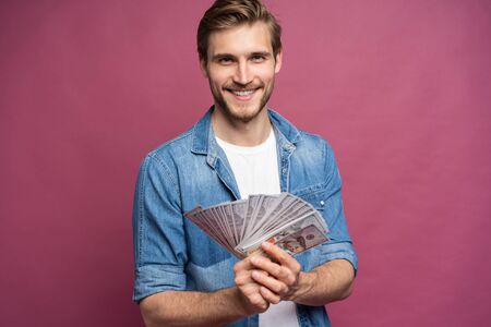 Portrait of a cheerful man holding dollar bills over pink background.の写真素材