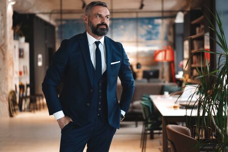 Stylish bearded man in a suit standing in modern officeの写真素材