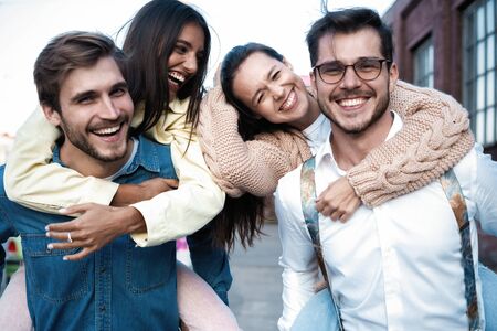 Two happy couple having fun piggyback ride outdoor, smiling happy, laughing togetherの写真素材