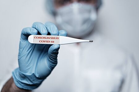 Closeup man in medical mask and glove holding thermometer with COVID-19 text. Coronavirus symptoms diagnosis. Corona virus pandemic. Concept of Corona virus quarantine, Covid-19の写真素材