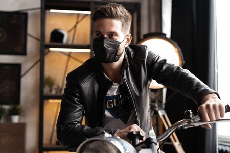 Handsome brutal male biker in black mask in leather jacket sitting on motorcycle looking forward.の写真素材