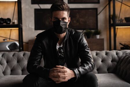 Handsome young manin black mask. Fashionable man in leather jacket standing and looking at windowの写真素材