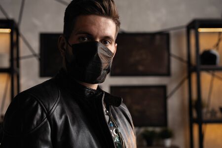 Handsome young manin black mask. Fashionable man in leather jacket standing and looking at windowの写真素材