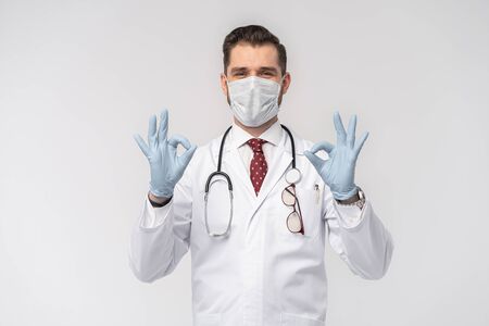 Coronavirus. COVID-19 pandemic. Attractive handsome doctor in protective face mask, white lab coat isolated on whiteの写真素材