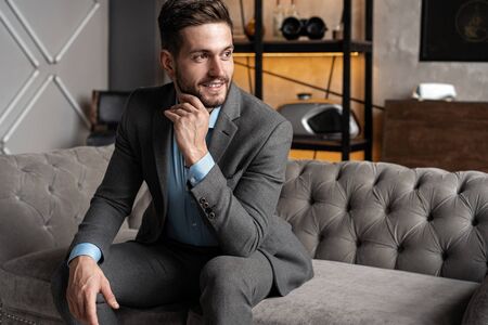 Cool and handsome. Good looking young man in full suit sitting on the sofa while spending time...