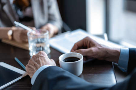Close up photo of man holding a cup of coffee and his business partner, in a restaurant during business lunch.の写真素材