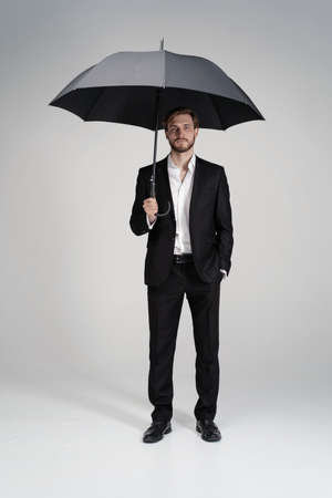 Businessman in a suit standing under black umbrella.の写真素材