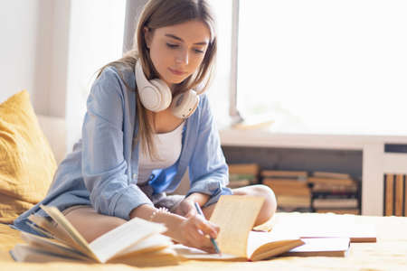 Attractive student woman laying on her bed at home while writing and working on her homework from...