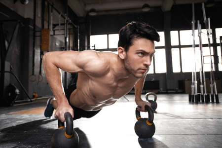 Handsome muscular man doing pushup exercise with dumbbell in a crossfit workout.