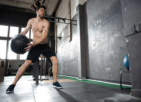 Young strong fit muscular man doing throwing medicine ball up on the wall for crossfit training hard...
