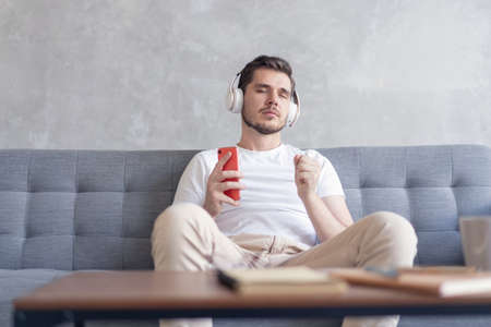 Enjoying his favorite music. Cheerful young man in headphones listening to the music while sittng on...