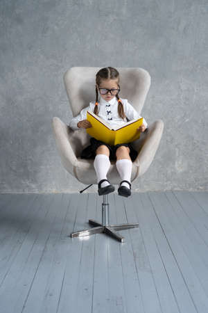 School girl focused on reading book sit in armchair.の写真素材