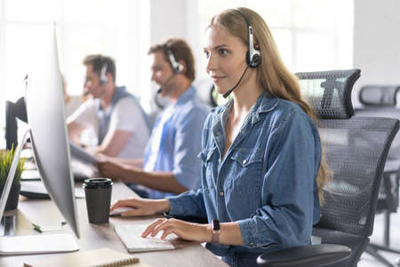 How can I help you? Beautiful call center workers in headphones are working at modern office