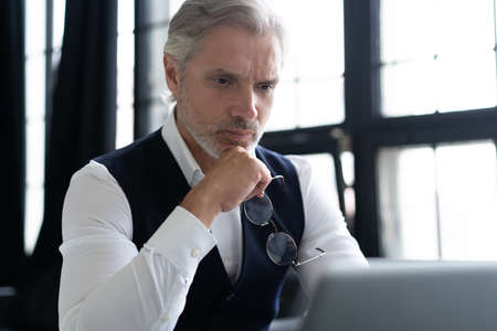 Concentrated at work. Mature man in full suit using laptop while working in modern office.の写真素材