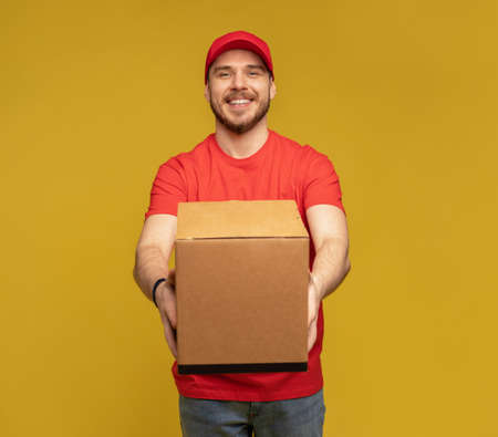 Delivery man with box in studio isolated on yellow background.の写真素材