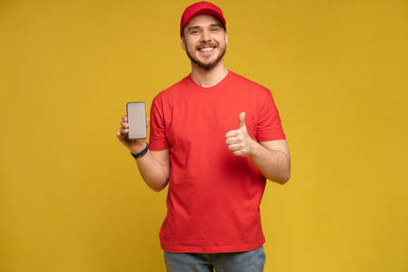 Young man holding smartphone isolated on yellow.